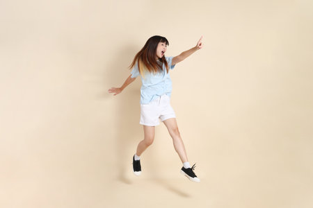 Young Asian woman wearing a light blue polo shirt, and white shorts, Jumping against a plain beige background. College student, Gen Z, Summerの写真素材
