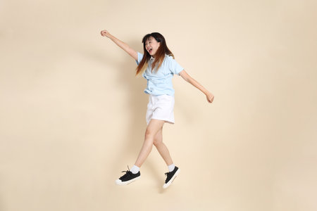 Young Asian woman wearing a light blue polo shirt, and white shorts, Jumping against a plain beige background. College student, Gen Z, Summerの写真素材