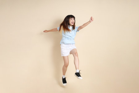 Young Asian woman wearing a light blue polo shirt, and white shorts, Jumping against a plain beige background. College student, Gen Z, Summerの写真素材