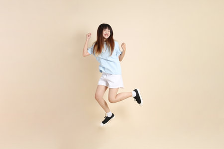 Young Asian woman wearing a light blue polo shirt, and white shorts, Jumping against a plain beige background. College student, Gen Z, Summerの写真素材