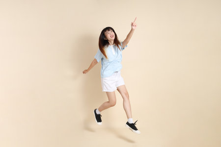 Young Asian woman wearing a light blue polo shirt, and white shorts, Jumping against a plain beige background. College student, Gen Z, Summerの写真素材