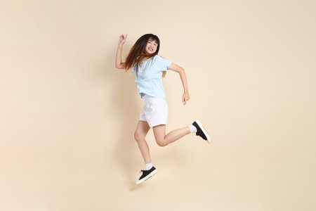 Young Asian woman wearing a light blue polo shirt, and white shorts, Jumping against a plain beige background. College student, Gen Z, Summerの写真素材