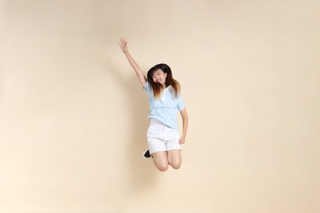Young Asian woman wearing a light blue polo shirt, and white shorts, Jumping against a plain beige background. College student, Gen Z, Summerの写真素材