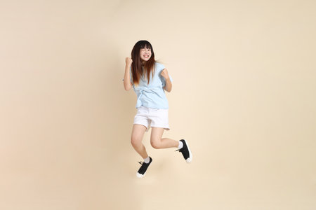 Young Asian woman wearing a light blue polo shirt, and white shorts, Jumping against a plain beige background. College student, Gen Z, Summerの写真素材