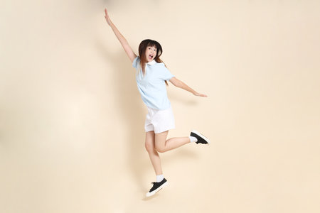 Young Asian woman wearing a light blue polo shirt, and white shorts, Jumping against a plain beige background. College student, Gen Z, Summerの写真素材