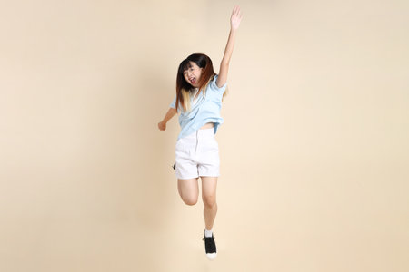 Young Asian woman wearing a light blue polo shirt, and white shorts, Jumping against a plain beige background. College student, Gen Z, Summerの写真素材