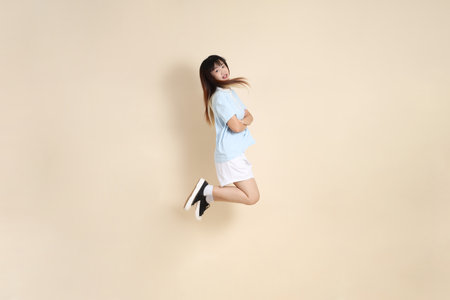 Young Asian woman wearing a light blue polo shirt, and white shorts, Jumping against a plain beige background. College student, Gen Z, Summerの写真素材