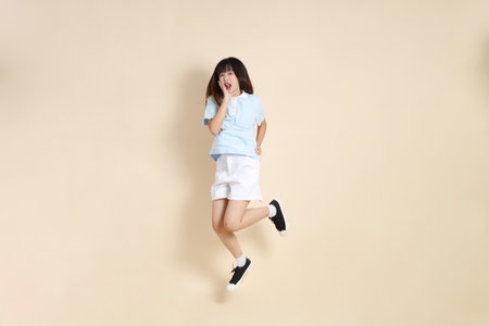 Young Asian woman wearing a light blue polo shirt, and white shorts, Jumping against a plain beige background. College student, Gen Z, Summerの写真素材