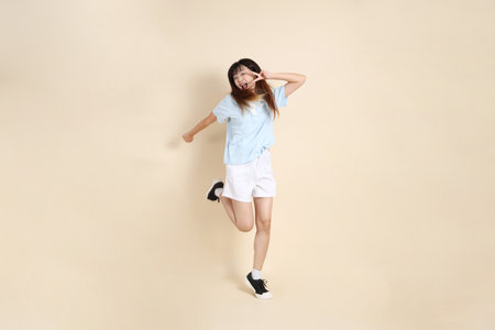 Young Asian woman wearing a light blue polo shirt, and white shorts, Jumping against a plain beige background. College student, Gen Z, Summerの写真素材