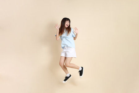 Young Asian woman wearing a light blue polo shirt, and white shorts, Jumping against a plain beige background. College student, Gen Z, Summerの写真素材