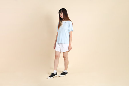 Young Asian woman wearing a light blue polo shirt, and white shorts, Walking against a plain beige background. College student, Gen Z, Summerの写真素材