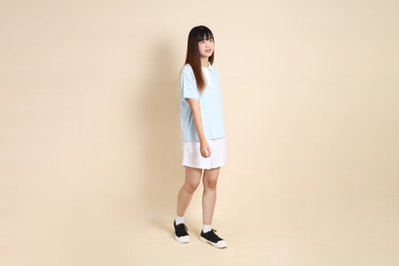 Young Asian woman wearing a light blue polo shirt, and white shorts, Walking against a plain beige background. College student, Gen Z, Summerの写真素材