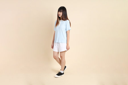 Young Asian woman wearing a light blue polo shirt, and white shorts, Walking against a plain beige background. College student, Gen Z, Summerの写真素材