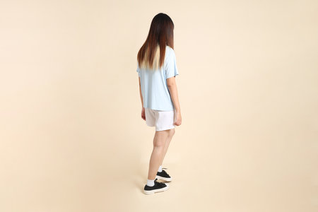 Young Asian woman wearing a light blue polo shirt, and white shorts, Walking against a plain beige background. College student, Gen Z, Summerの写真素材