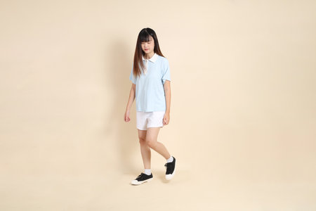 Young Asian woman wearing a light blue polo shirt, and white shorts, Walking against a plain beige background. College student, Gen Z, Summerの写真素材