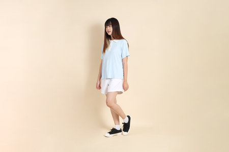 Young Asian woman wearing a light blue polo shirt, and white shorts, Walking against a plain beige background. College student, Gen Z, Summerの写真素材