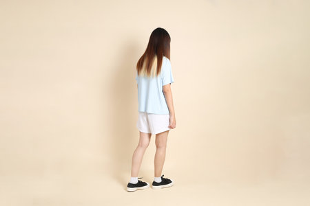 Young Asian woman wearing a light blue polo shirt, and white shorts, Walking against a plain beige background. College student, Gen Z, Summerの写真素材
