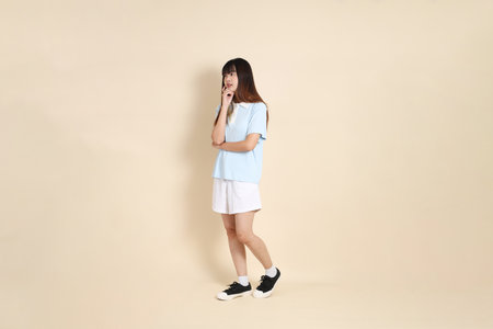 Young Asian woman wearing a light blue polo shirt, and white shorts, Walking against a plain beige background. College student, Gen Z, Summerの写真素材