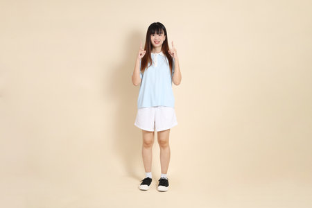Young Asian woman wearing a light blue polo shirt, and white shorts, pointing against a plain beige background. College student, Gen Z, Summerの写真素材
