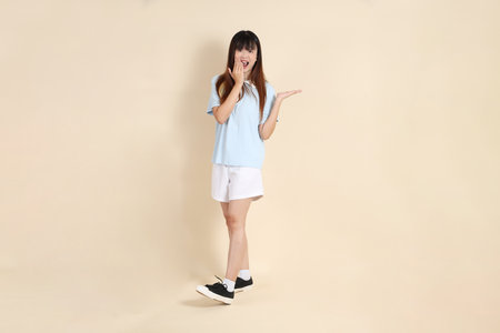 Young Asian woman wearing a light blue polo shirt, and white shorts, pointing against a plain beige background. College student, Gen Z, Summerの写真素材