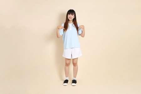 Young Asian woman wearing a light blue polo shirt, and white shorts, pointing against a plain beige background. College student, Gen Z, Summerの写真素材