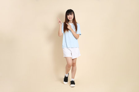 Young Asian woman wearing a light blue polo shirt, and white shorts, pointing against a plain beige background. College student, Gen Z, Summerの写真素材