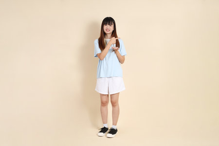 Young Asian woman wearing a light blue polo shirt, and white shorts, pointing against a plain beige background. College student, Gen Z, Summerの写真素材