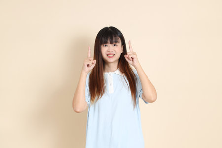 Young Asian woman wearing a light blue polo shirt, pointing against a plain beige background. College student, Gen Z, Summerの写真素材