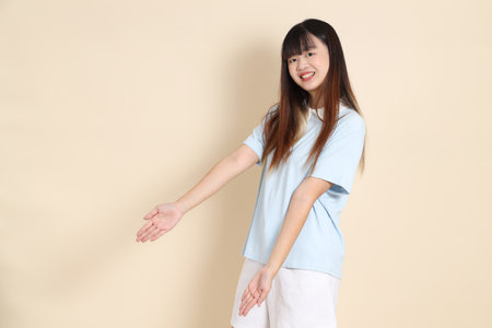 Young Asian woman wearing a light blue polo shirt, and white shorts, pointing against a plain beige background. College student, Gen Z, Summerの写真素材
