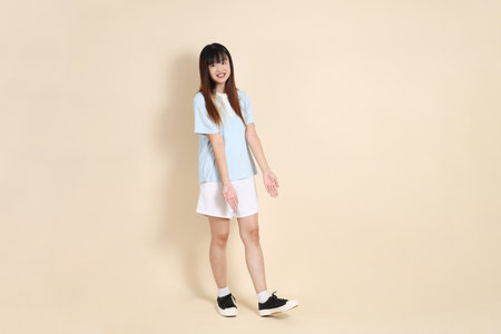 Young Asian woman wearing a light blue polo shirt, and white shorts, pointing against a plain beige background. College student, Gen Z, Summerの写真素材