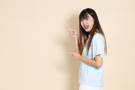 Young Asian woman wearing a light blue polo shirt, and white shorts, pointing against a plain beige background. College student, Gen Z, Summerの写真素材