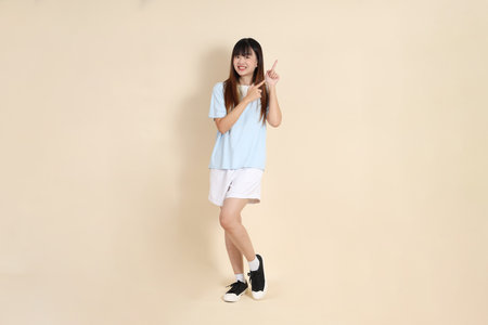 Young Asian woman wearing a light blue polo shirt, and white shorts, pointing against a plain beige background. College student, Gen Z, Summerの写真素材