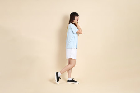 Young Asian woman wearing a light blue polo shirt, and white shorts, pointing against a plain beige background. College student, Gen Z, Summerの写真素材