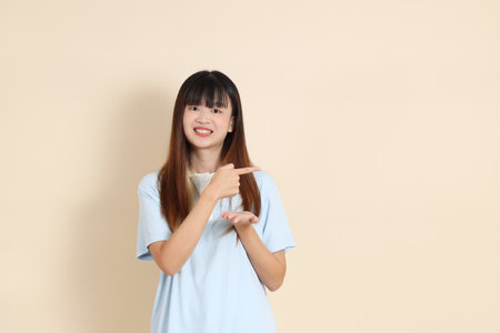 Young Asian woman wearing a light blue polo shirt, pointing against a plain beige background. College student, Gen Z, Summerの写真素材