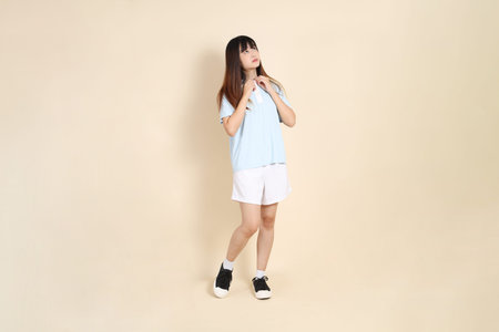 Young Asian woman wearing a light blue polo shirt, and white shorts, get dressed against a plain...