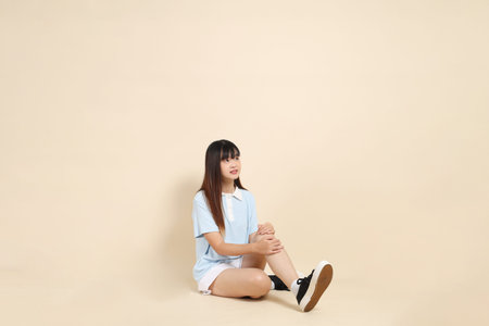 Young Asian woman wearing a light blue polo shirt, and white shorts, sitting against a plain beige background. College student, Gen Z, Summerの写真素材