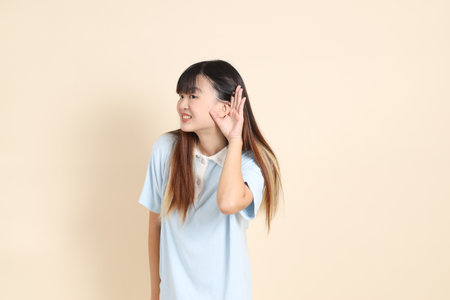 Young Asian woman wearing a light blue polo shirt, and white shorts, Listening or hearing against a plain beige background. College student, Gen Z, Summerの写真素材