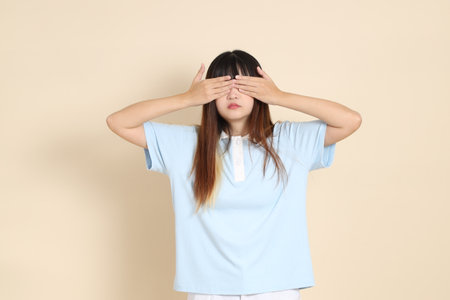 Young Asian woman wearing a light blue polo shirt, and white shorts, Cover eyes against a plain beige background. College student, Gen Z, Summerの写真素材