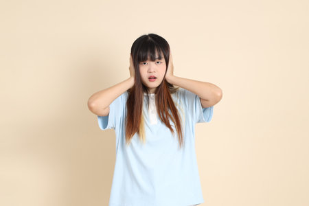 Young Asian woman wearing a light blue polo shirt, and white shorts, ear close against a plain beige background. College student, Gen Z, Summerの写真素材