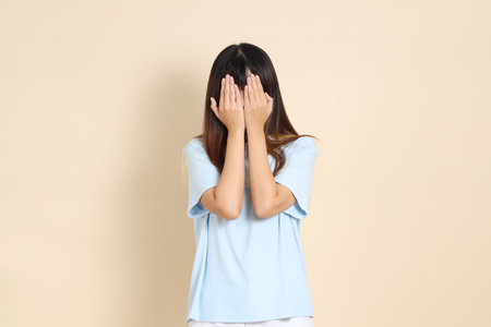 Young Asian woman wearing a light blue polo shirt, and white shorts, Cover eyes against a plain beige background. College student, Gen Z, Summerの写真素材