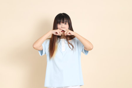 Young Asian woman wearing a light blue polo shirt, and white shorts, Mouth close, Silent gesture against a plain beige background. College student, Gen Z, Summerの写真素材