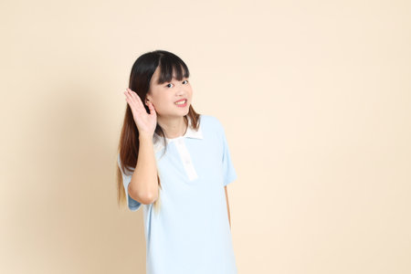 Young Asian woman wearing a light blue polo shirt, and white shorts, Listening or hearing against a plain beige background. College student, Gen Z, Summerの写真素材