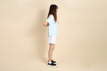 Young Asian woman wearing a light blue polo shirt, and white shorts, backache against a plain beige background. College student, Gen Z, Summerの写真素材