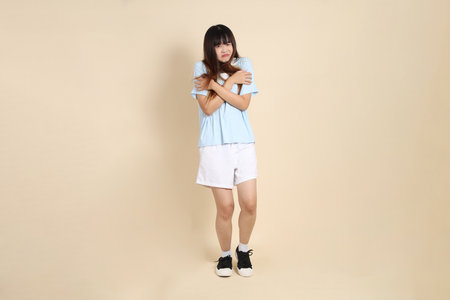 Young Asian woman wearing a light blue polo shirt, and white shorts, Feeling cold against a plain beige background. College student, Gen Z, Summerの写真素材