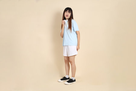 Young Asian woman wearing a light blue polo shirt, and white shorts, feeling hot against a plain beige background. College student, Gen Z, Summerの写真素材