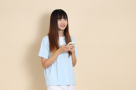 Young Asian woman wearing a light blue polo shirt, and white shorts, Holding mobile phone against a plain beige background. College student, Gen Z, Summerの写真素材