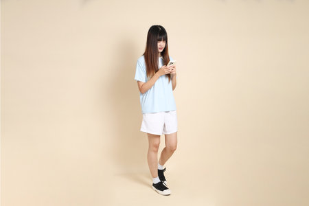 Young Asian woman wearing a light blue polo shirt, and white shorts, Holding mobile phone against a plain beige background. College student, Gen Z, Summerの写真素材