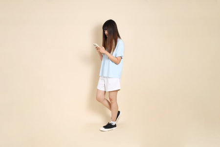 Young Asian woman wearing a light blue polo shirt, and white shorts, Holding mobile phone against a plain beige background. College student, Gen Z, Summerの写真素材