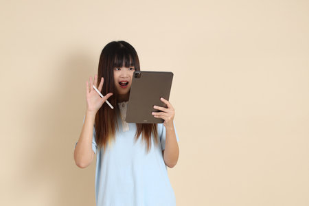 Young Asian woman wearing a light blue polo shirt, and white shorts, Holding tablet against a plain beige background. College student, Gen Z, Summerの写真素材