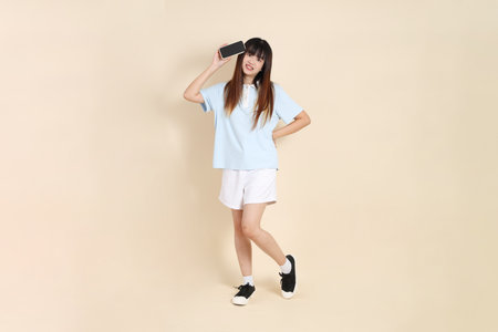 Young Asian woman wearing a light blue polo shirt, and white shorts, Holding mobile phone against a plain beige background. College student, Gen Z, Summerの写真素材